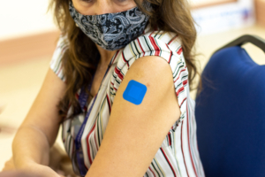 Woman in mask showing her arm with a blue bandaid where she received her vacciniation