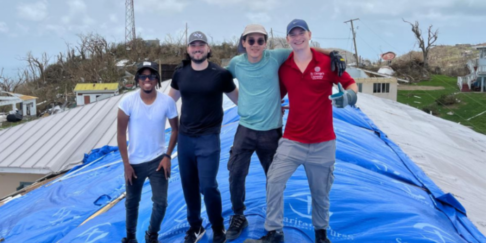 4 SGU students stand on a roof that they are helping repair.