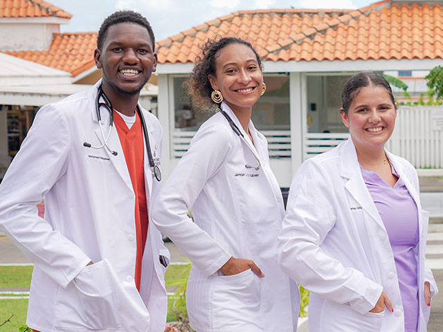 three students in white-coats on campus